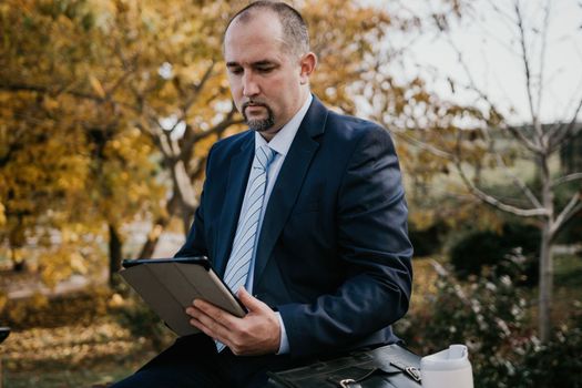 Mature entrepreneur drink coffee in autumn park. Senior executive rest in city park.