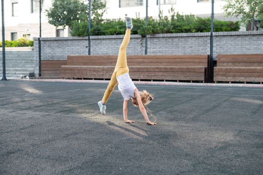 Caucasian girl makes a cartwheel on the sports field outdoors