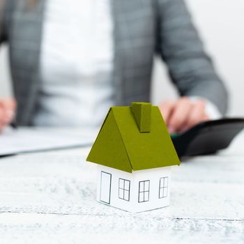 Businesswoman sitting and writing in notebook. Paper house' on desk.