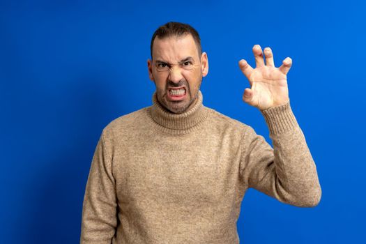 Bearded middle age man wearing turtleneck making claw gesture with obvious angry, aggressive and pensive expression