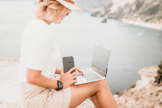Digital nomad, Business woman working on laptop by the sea. Pretty lady typing on computer by the sea at sunset, makes a business transaction online from a distance. Freelance remote work on vacation