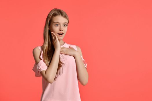 Studio portrait of a nice blonde schoolgirl with a long hair, in a rosy t-shirt, standing against a pink background in various poses. She expresses different emotions posing right in front of the camera, smiling and looking wondered.