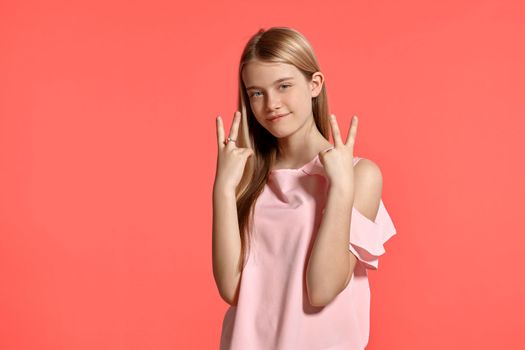 Studio portrait of a lovely blonde teenager with a long hair, in a rosy t-shirt, standing against a pink background in various poses. She expresses different emotions posing right in front of the camera, smiling and gesticulating.
