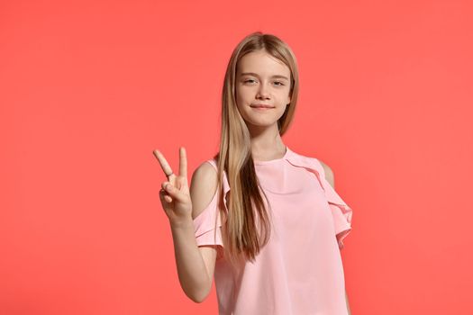 Studio portrait of an attractive blonde adolescent with a long hair, in a rosy t-shirt, standing against a pink background in various poses. She expresses different emotions posing right in front of the camera, smiling and looking happy.