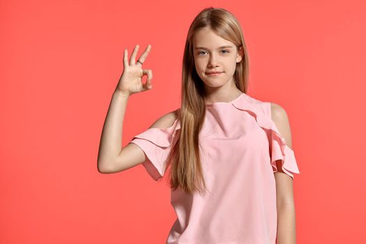 Studio portrait of a beautiful blonde adolescent with a long hair, in a rosy t-shirt, standing against a pink background in various poses. She expresses different emotions posing right in front of the camera, smiling and showing okay sign.