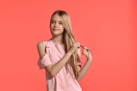 Studio portrait of a cute blonde young lady with a long hair, in a rosy t-shirt, standing against a pink background in various poses. She expresses different emotions posing right in front of the camera, smiling and touching her hair.