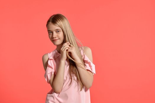 Studio portrait of a cute blonde adolescent with a long hair, in a rosy t-shirt, standing against a pink background in various poses. She expresses different emotions posing right in front of the camera, smiling and stroking hair.