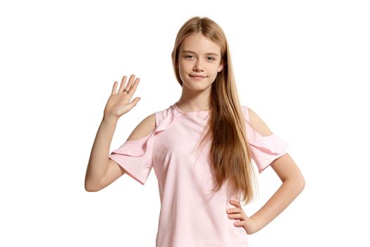 Studio portrait of a lovely blonde adolescent in a pink t-shirt isolated on white background in various poses. She expresses different emotions posing right in front of the camera, smiling and waving her hand.