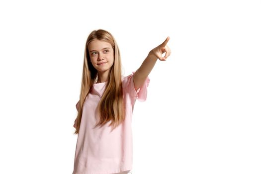 Studio portrait of a pretty blonde teenager in a pink t-shirt isolated on white background in various poses. She expresses different emotions posing right in front of the camera, looking up and pointing on something.