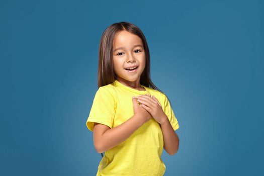 little girl in yellow t-shirt hands on her heart on the blue background