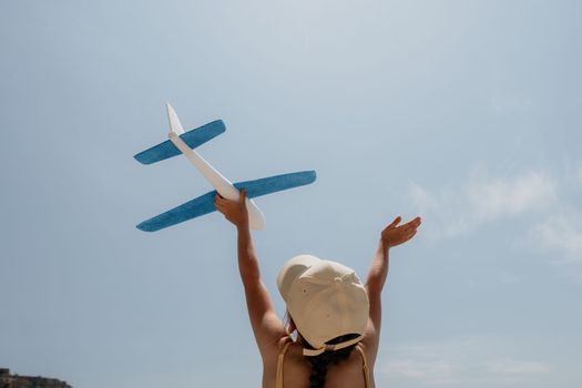 Kid playing with toy airplane. Children dream of travel by plane. Happy child girl has fun in summer vacation by sea and mountains. Outdoors activities at background of blue sky. Lifestyle moment