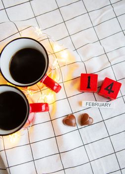 Two cups of coffee in red cups on a background of chocolate canfet in the form of a heart. Morning surprise for Valentine's Day. View from above