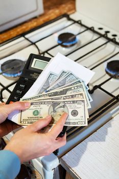 Payment of utility bills, calculations on a calculator. Euro and dollar bills lie near a burning gas burner. The concept of increasing the cost of natural gas supply and payment. Energy crisis, vertical photo