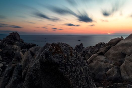 rocky coast seascape, sunset sun shines orange in the blue sky with few clouds, relaxing feeling of peace and tranquility. Long exposure. Capo Testa, Santa Teresa di Gallura, Sardinia, Italy