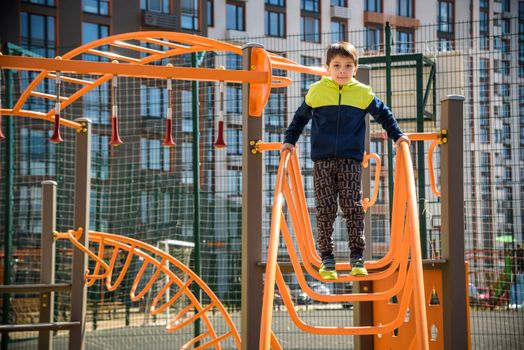 Cute boy is climbing on the playground in the schoolyard. He has a very happy face and enjoy this adventure sports alone outdoor. Warm sunny day.