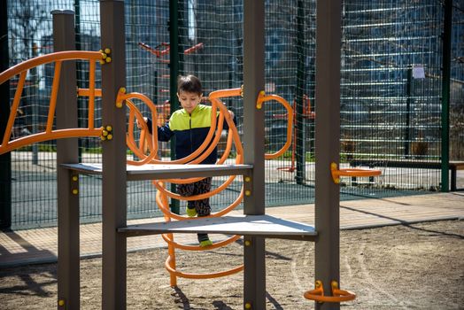 Cute boy is climbing on the playground in the schoolyard. He has a very happy face and enjoy this adventure sports alone outdoor. Warm sunny day.