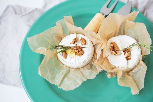 Baked camembert with walnuts, honey and rosemary wrapped in parchment lies on a green plate, delicious and healthy food. View from above