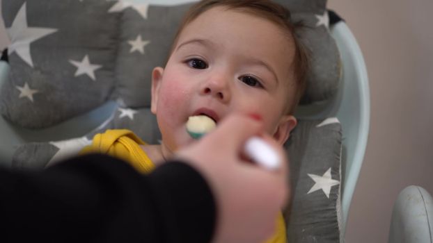 A little boy sits on a chair and is fed from a spoon. The child eats porridge. 4k