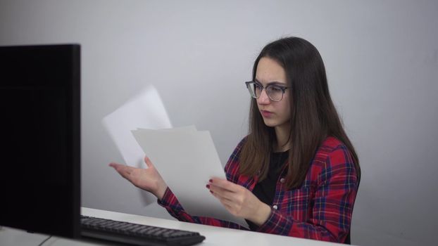 A young IT lady reads documents and throws them out of anger. A woman is sitting at the workplace in the office. Girl in a red shirt and glasses. 4k