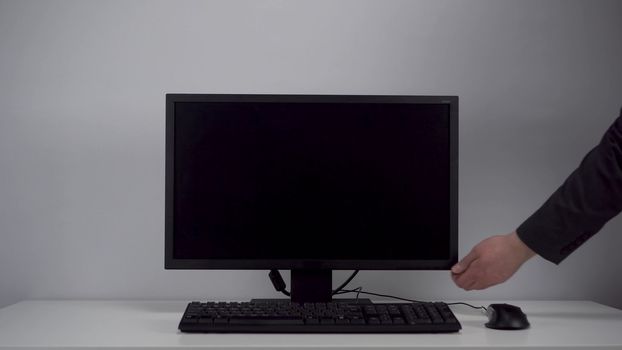 Turning on the monitor with a green screen. A man with his hand turns on the computer screen on the desktop in the office. Chroma key. 4k