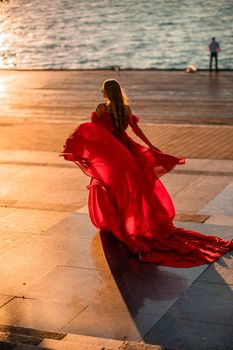 Sunrise red dress. A woman in a long red dress against the backdrop of sunrise, bright golden light of the sun's rays. The concept of femininity, harmony