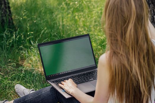 girl sits on the grass and works at a laptop. freelance. selfeducation. the concept of distance learning outdoors