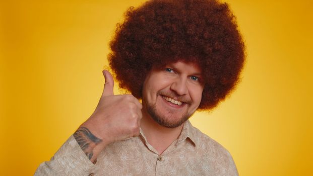 Like. Bearded man with lush Afro hairstyle coiffure raises thumbs up agrees with something, gives positive reply recommends advertisement likes good. Young hipster guy on yellow studio background
