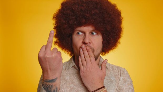 Aggressive crazy hooligan man showing around his middle fingers, demonstrating protest with impolite rude gesture of disrespect, rejecting communication. Hipster guy with lush afro hairstyle coiffure