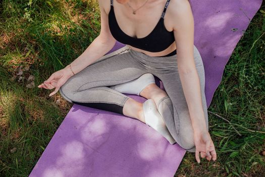 Yoga woman on green grass girl relaxes in the field. Yoga woman in green park girl doing gymnastics outdoors. Meditating woman in meditation in yoga pose practices outdoors