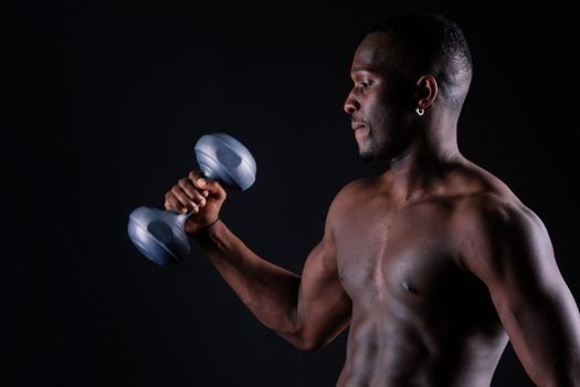 Confident young man shirtless portrait training with dumb-bell against black background.