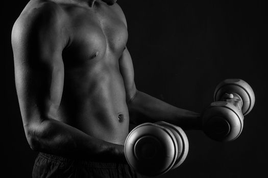 Confident young man shirtless portrait training with dumb-bell against black background.