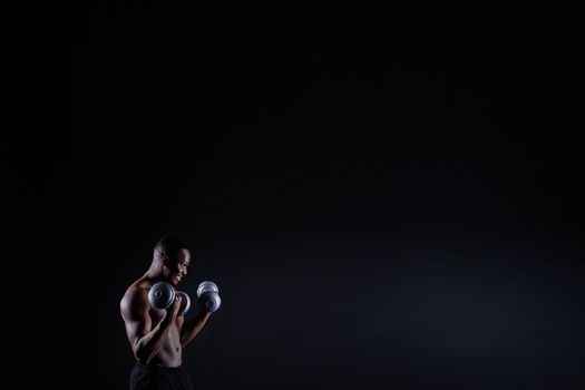 Confident young man shirtless portrait training with dumb-bell against black background.