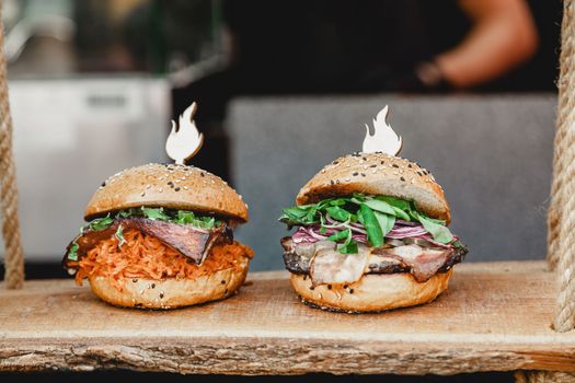 Delicious burgers on a wooden base. Two delicious homemade burgers of beef, cheese and vegetables on an old wooden table. Fat unhealthy food close-up. Burger fest.