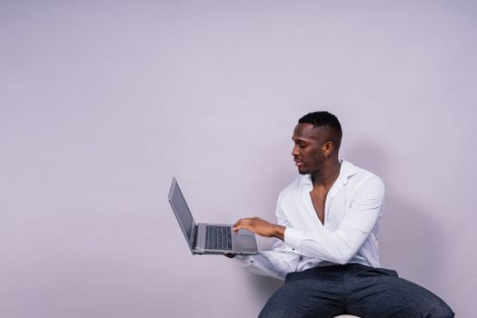 Optimistic african-american male student in a casual shirt using laptop pc isolated