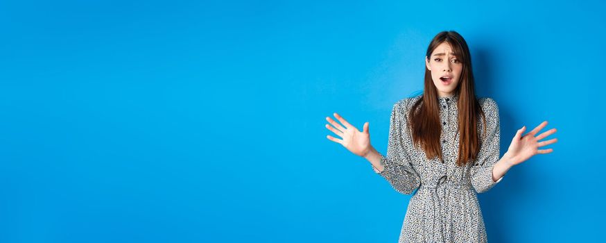 Sad and gloomy woman in dress facing failure, looking distressed and sighing upset, losing and standing on blue background.