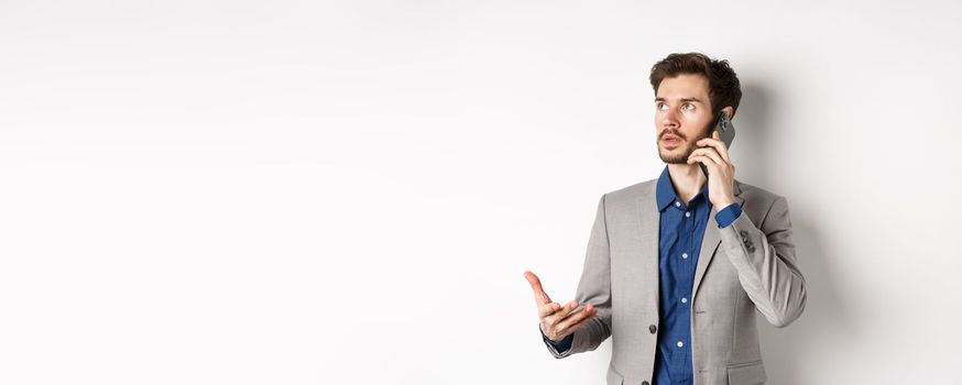 Businessman making phone call, talking on smartphone and looking busy, wearing suit, white background.