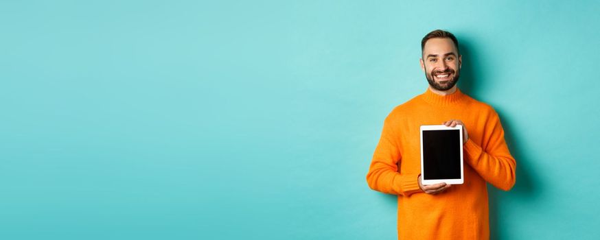 Technology. Smiling handsome man showing digital tablet screen, demonstrating application, standing over turquoise background.