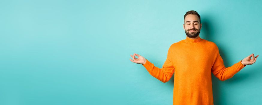 Image of relaxed and relieved man close eyes and smiling, feeling stress-free, meditating with calm expression, standing over light blue background.