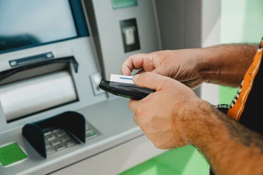 Man ATM card. ATM insert card. Man putting credit card in atm machine while holding wallet.