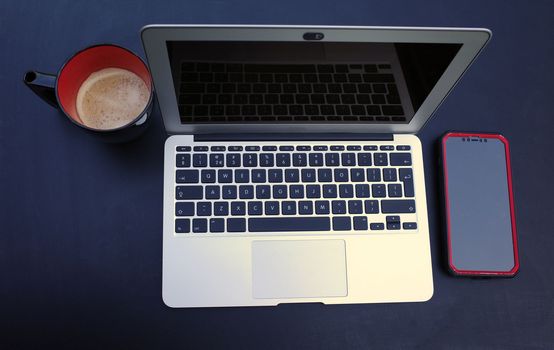 Top view on a working place with laptop, smartphone and black and red mug with coffee