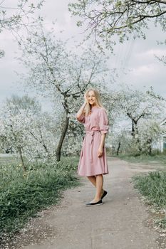 Blonde girl on a spring walk in the garden with cherry blossoms. Female portrait, close-up. A girl in a pink polka dot dress