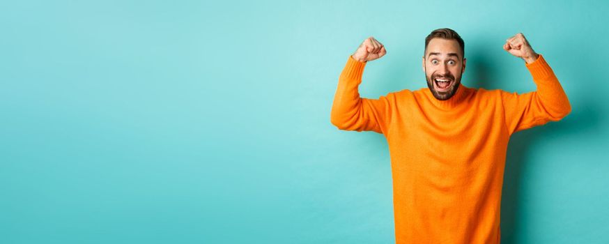 Handsome man celebrating victory, winning and looking happy, triumphing over win, standing over light blue background.