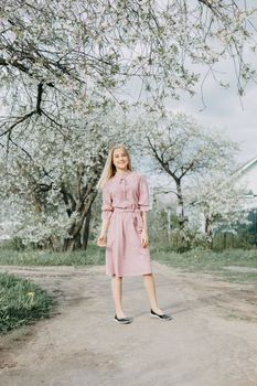 Blonde girl on a spring walk in the garden with cherry blossoms. Female portrait, close-up. A girl in a pink polka dot dress