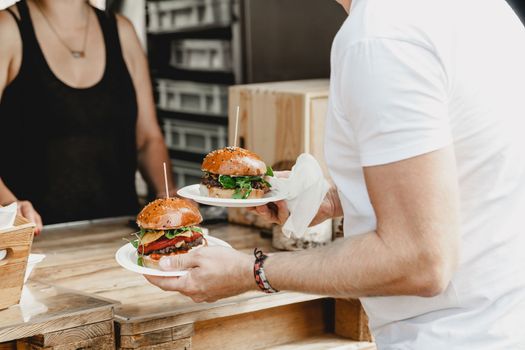 Man holds in his hand burgers at a burger feast. Dinner Hamburger Food Feast Party. Big burger in hands at street food outdoor festival. Festival food day.
