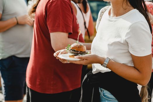 Woman holds in his hand burgers at a burger feast. Dinner Hamburger Food Feast Party. Big burger in hands at street food outdoor festival. Festival food day.