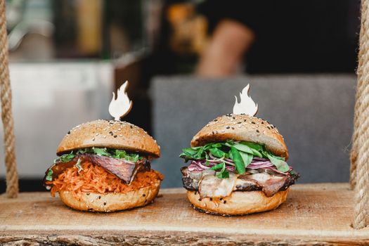 Delicious burgers on a wooden base. Two delicious homemade burgers of beef, cheese and vegetables on an old wooden table. Fat unhealthy food close-up. Burger fest.