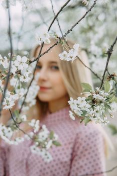 Blonde girl on a spring walk in the garden with cherry blossoms. Female portrait, close-up. A girl in a pink polka dot dress