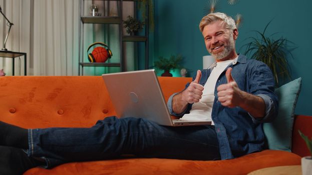 Like gesture. Surprised mature man use laptop computer, receive good news message, shocked by sudden victory, celebrate win, lottery jackpot, purchases online shopping at home. Lifestyle technologies