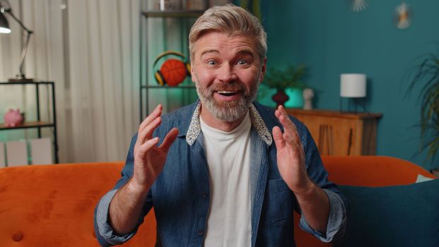 Oh my God, Wow. Surprised middle-aged senior man at home couch, shocked by sudden victory triumph, good win news, celebrating lottery jackpot luck. Excited amazed mature old guy in night evening room