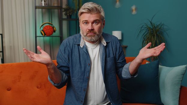 I dont know what to say. Confused middle-aged man feeling embarrassed about ambiguous question, having doubts, no idea, being clueless, uncertain at home. Mature senior gray-haired guy at night room